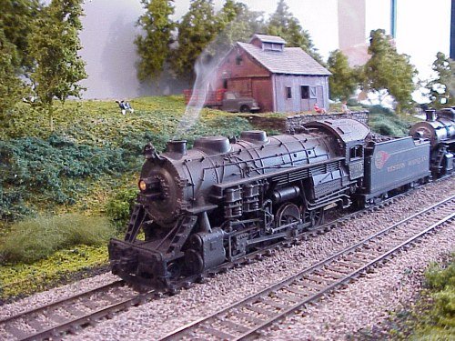 Karl Bond's WM consolidation is really belching smoke in this image. No, the webmaster
didn't retouch this one. Karl's rejuvinated this older Bachmann model, and runs the smoke
unit from the DCC decoder! This scene is on Jim McLaughlin's re-sceniced farm module
(see our Module Make-Over <meeting0402.htm> from a couple of months back).
